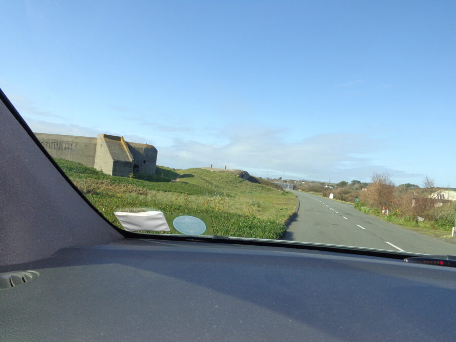 A large concrete bunker seen through the window of a car. Located on the west coast of Guernsey. This World War Two bunker would have contained several machine gun positions.