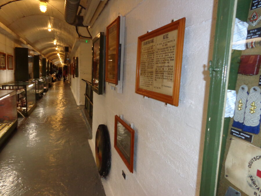 A long white-painted corridor in La Valette Underground Military Museum. It is lined with display cases and framed items.