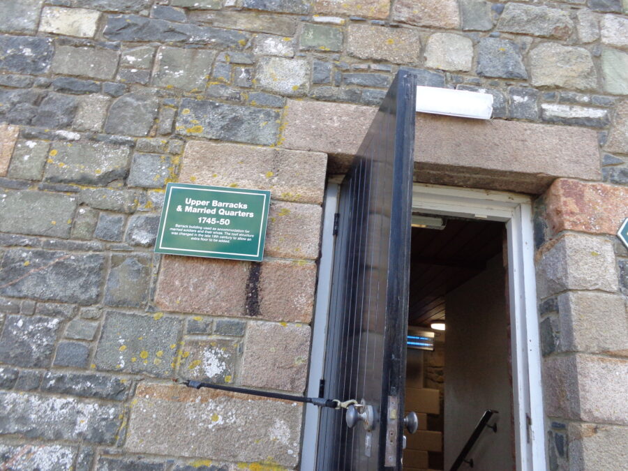 A black painted doorway in a stone wall leading into the Upper Barracks. According to a sign that can be seen the building dates from 1745-50. The Upper Barracks was used as accommodation for married soldiers and their families. The interior was changed in the 19th century to allow an extra floor to be added.