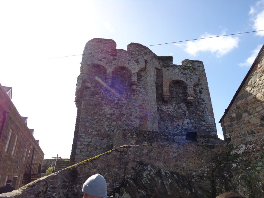 An old stone tower at Castle Cornet. Its appearance suggests it might be medieval. Newer stone buildings are partly visible at either side.
