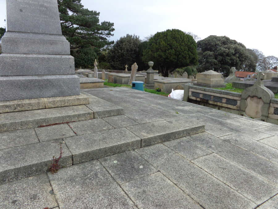 A substantial stone monument with a central plinth at Candie Cemetery. The inscription on the plinth is mostly out of view. Beyond are rows of raised stone tombs mixed with more ordinary grave stones.