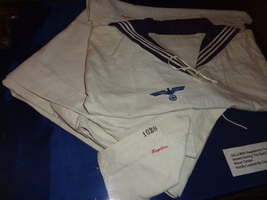 A white German Navy uniform displayed at the German Naval Signals Headquarters museum. The shirt is embroidered with eagle and swastika insignia. There is an arm band embroidered with number "1028" and the name "Haagedorn". This uniform dates from World War II when the Channel Islands were under German occupation. The uniform belonged to Oberleutnant Willi Hagedorn. Oberleutnant zur See is the highest rank of Lieutenant in the German Navy. 