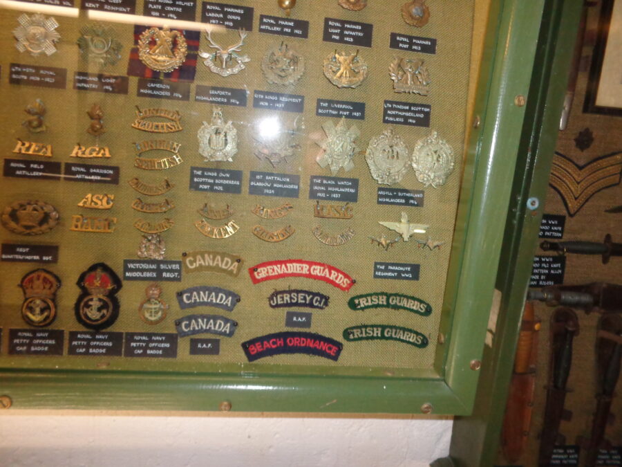British and Commonwealth military epaulettes and cap badges in a display case. The labels indicate these items date from between the late-19th century and the 1930s.