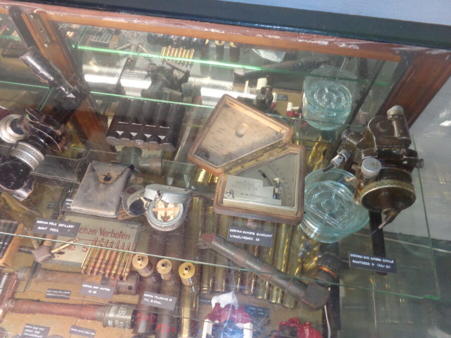 A display case containing various small items of German military equipment dating from World War II. It includes a compass, a gunner's quadrant and mine igniters.