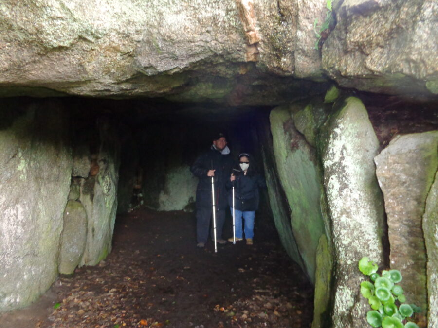 Looking into Le Creux ès Faies passage tomb with Tony and Tatiana inside. A huge slab of rock spans the entrance to the tomb.