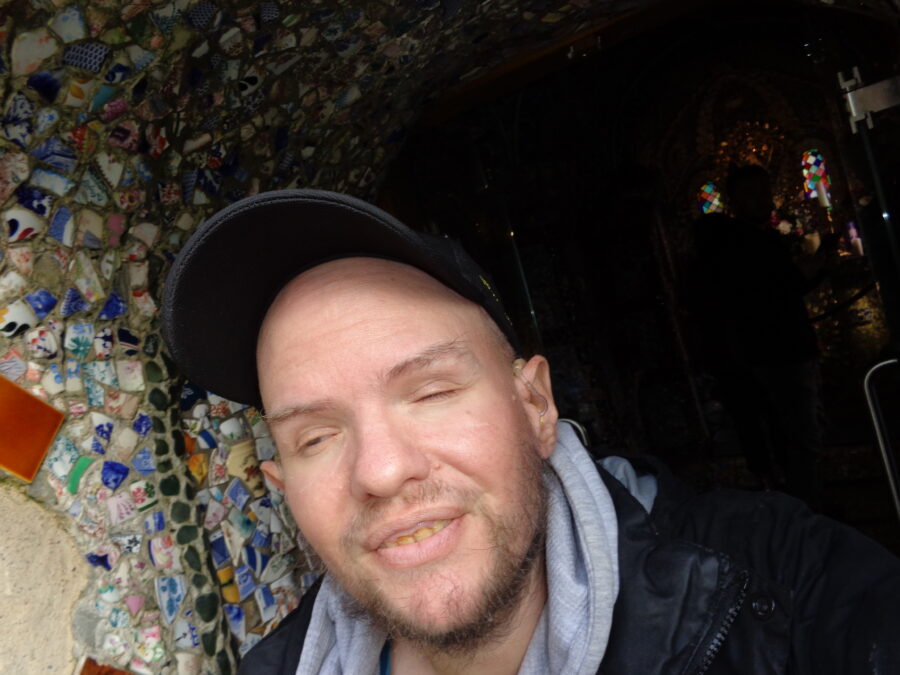 Tony in the doorway of the Little Chapel. The doorway is decorated with a colourful mosaic of pottery fragments.