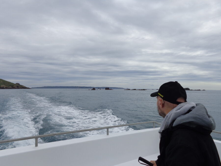Tony on the ferry returning to Guernsey from Sark. Various islands and rocks can be seen. The more distant island to the right is probably Sark and the closer land is probably the island of Herm along with surrounding small islets and rocks.