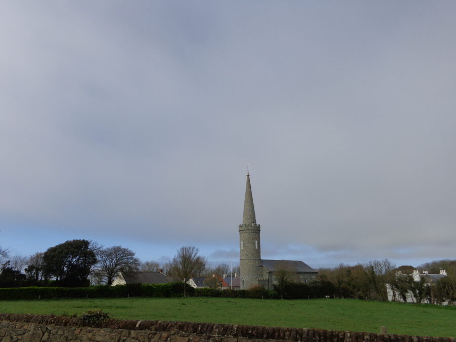 View towards Torteval Parish Church. This church was designed by John Wilson and built in 1818. It has a round tower with a tall spire on top. This is the tallest steeple in Guernsey and was intended to be used as a sea mark. The present structure was built on the site on an older church which had fallen into disrepair. The original church was consecrated in 1140. The church houses the oldest bell in the Channel Islands dating from 1432.