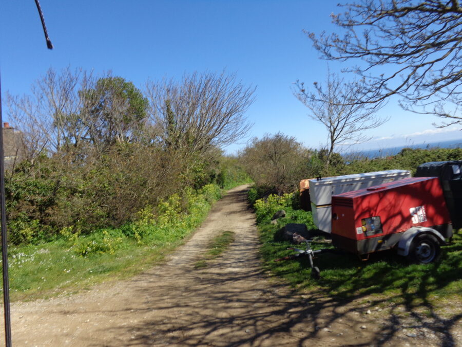 View from the horse and carriage heading down a lane lined with trees and bushes. To the right the sea is visible is the distance.