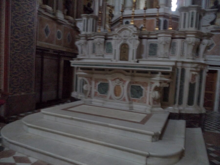 A closer view of the elaborately carved side altar. There are lots of curved motifs, some with floral designs, as well as inlaid marble panels. A row of gold candlesticks sits above.