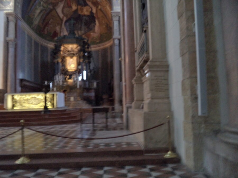 The golden main altar of Messina Cathedral. The photo is blurred but clear enough to show the main details. The half-domed ceiling is decorated with a large mosaic depicting Christ seated in a throne in the centre.