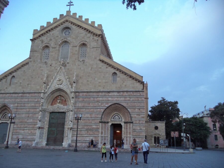 The front façade of Messina Cathedral, which is clad in marble. This façade is largely symmetrical with three arched doorways: a large central doorway and two slightly smaller ones at each side. The doorways are all richly decorated with bas-relief carving. The photo is too distant to show this in detail.