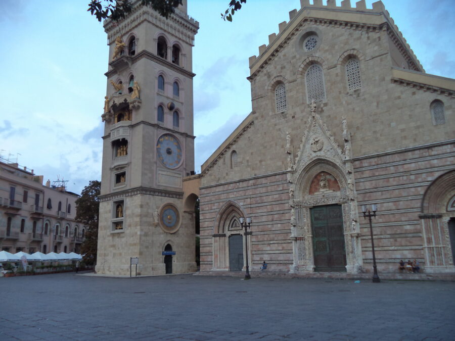 The bell tower and astronomical clock adjoining the left side of Messina Cathedral's front façade. The photo shows golden statues and other decoration in several tiers going up the tower. At the bottom there is a carousel depicting the days of the week: Friday is shown by Venus driving a dove. Other parts include a carousel of the ages of life, Biblical scenes that change in each quarter of the liturgical year, and at the top, a crowned lion (the symbol of Messina Province) which at midday waves the flag of Messina, moves its tail, turns its head and roars three times.