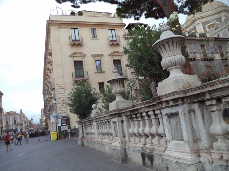 Looking the other way along the stone balustrade wall that encloses the cathedral garden. Decorative stone urns sit on top of the wall's pillars. Trees and bushes, some covered with bright flowers, can be seen within.