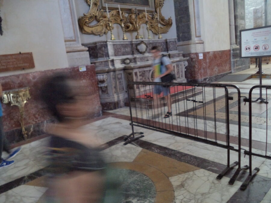 Another view inside Catania Cathedral. Possibly looking towards a side wall, which includes a mauve-purple marble altar with gold candlesticks on top. The elaborate golden frame of a large painting can be seen above (the painting itself is out of shot). The adjoining walls and floor are also clad in marble.