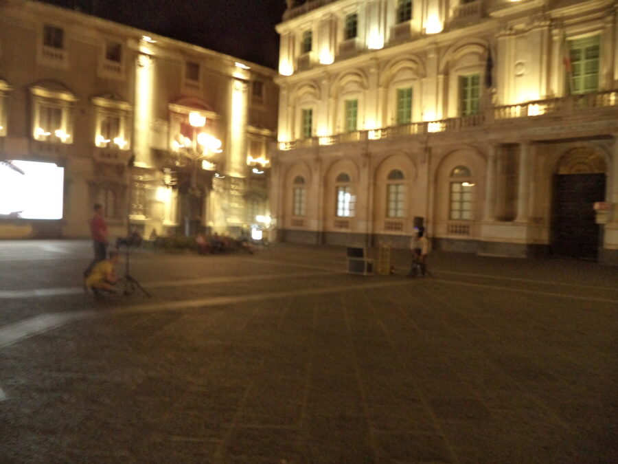 Evening view across Piazza dell Duomo, the main square of Catania. The historic buildings around the edges of the square are lit up in the semi-darkness.