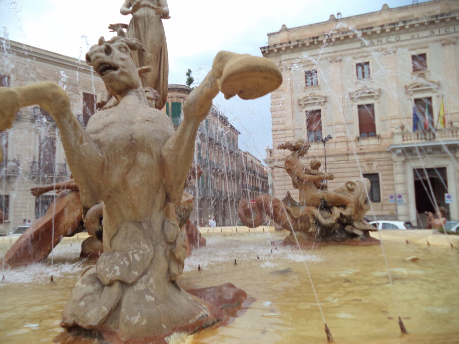 Another view of the atmospheric Fountain of Diana in Piazza Archimede. In the foreground a sea horse is depicted, its front legs rearing up out of the water. Further back to the right, a nude female figure holding a baby is carved sitting on top of a giant fish.