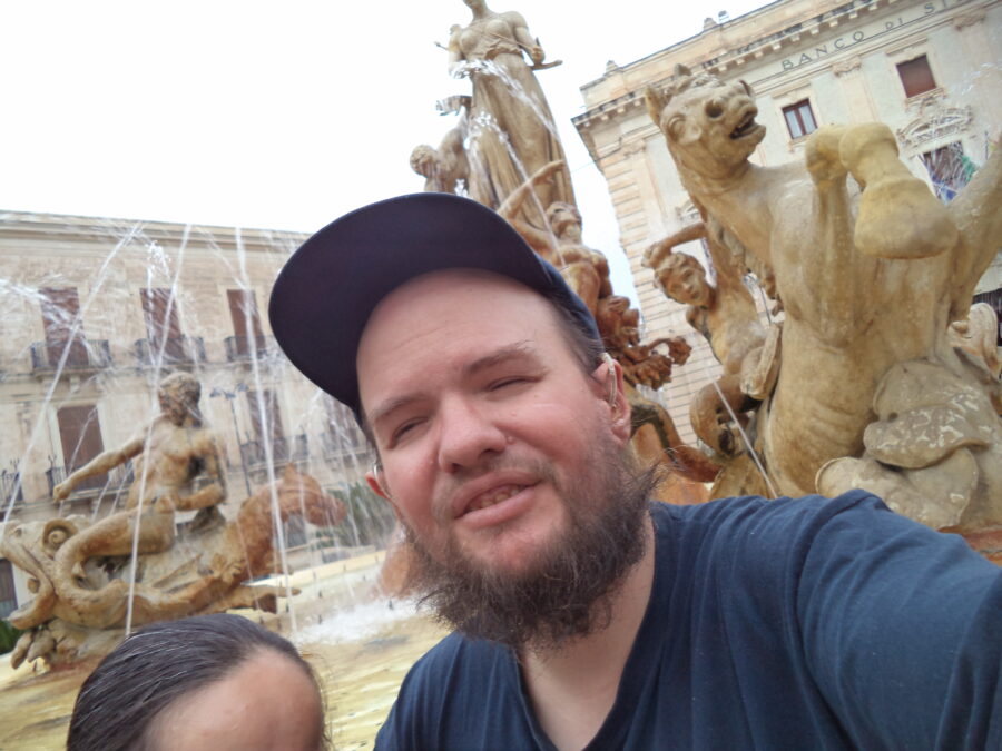 Tony and Tatiana in front of the Fountain of Diana. Only the top of Tatiana's head is in view. In the background most of the statue of Diana (or Artemis) can be seen on top of the central pedestal. Diana is carved holding a bow and arrow.