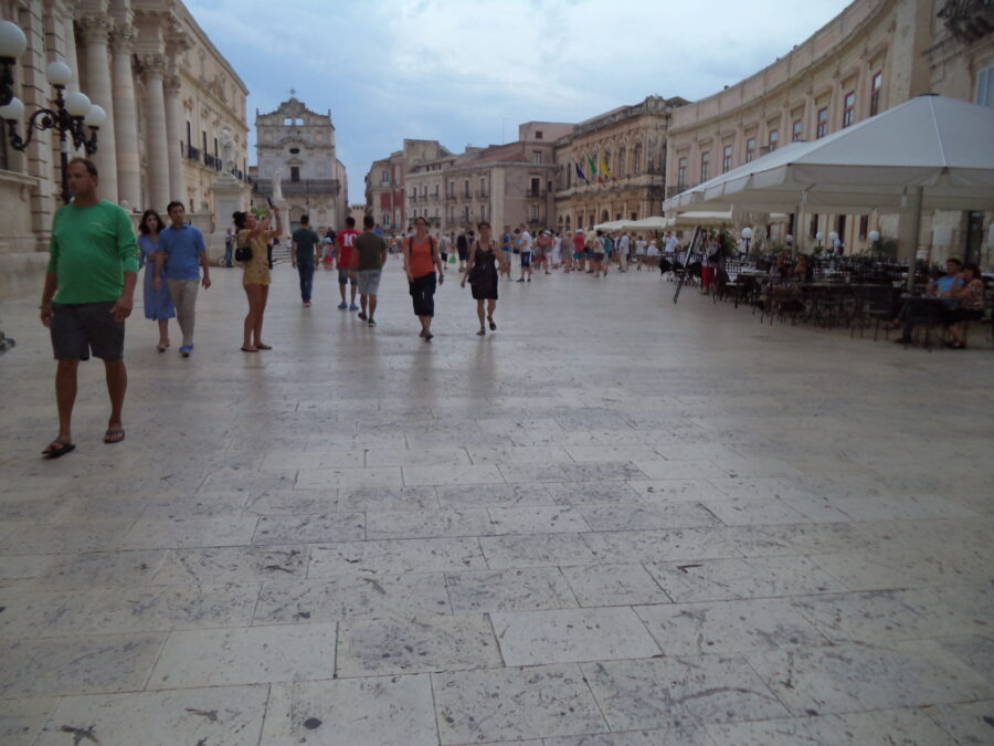 View across busy Piazza Duomo on Ortigia, the island that forms the historic centre of Syracuse. Syracuse Cathedral (Duomo di Siracusa) is the building with Corinthian columns partially visible to the left. This High Sicilian Baroque façade dates from 1725 to 1753 and was designed by Andrea Palma. The cathedral was rebuilt after the major earthquake in 1693. Another Baroque church is more clearly visible straight ahead at the south end of the square. This is the Church of Santa Lucia alla Badia. A church and monastery has existed here since at least the mid-15th century. The present church was completed in 1703 following the 1693 earthquake. The building is today deconsecrated and is used for special exhibitions and functions.
