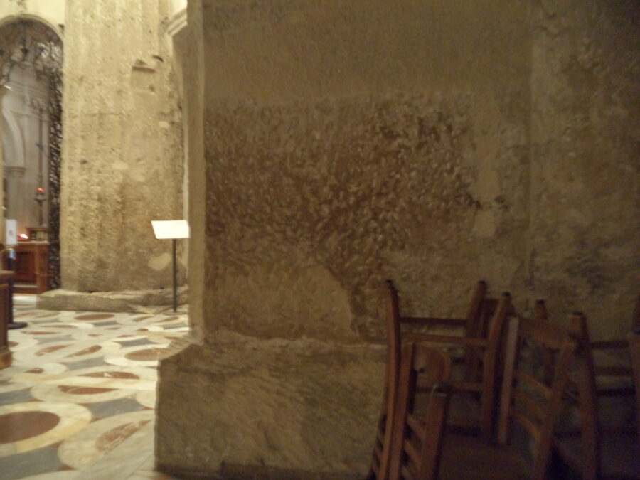 View of the bases of two massive worn and weathered stone columns inside Syracuse Cathedral. These likely date back to the Greek temple that once stood on this site.