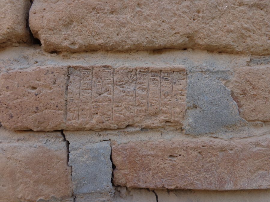 The face of a brick carved with an inscription located within one of the temples at Dur-Kurigalzu. The worn inscription is arranged in vertical lines and is written in an ancient cuneiform script.