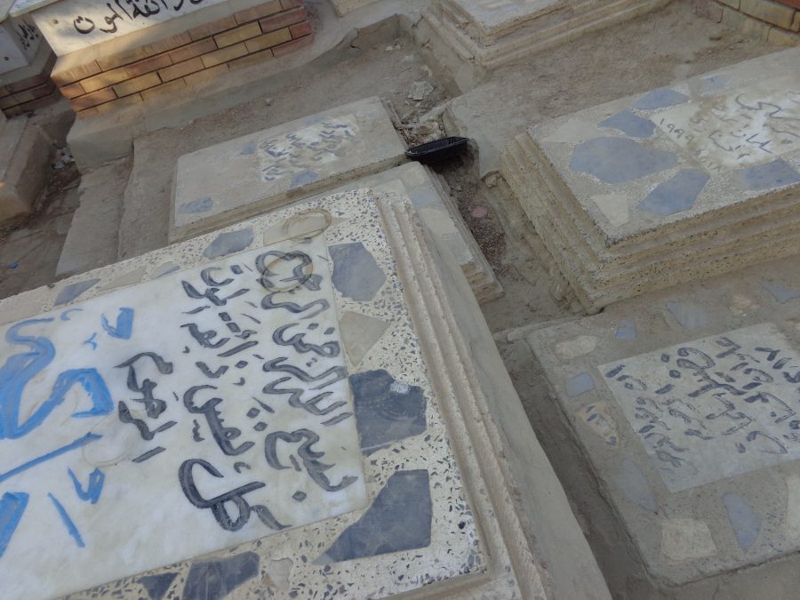 
7. Close-up view of a group of tombs in Wadi-us-Salaam cemetery, reputed to be the largest in the world. The tombs are grouped close together with only very narrows gaps around the sides. The tombs are typically topped with stone, often marble, with inscriptions in Arabic script. The sides of the tombs appear to be made variously of brick, concrete or stone.