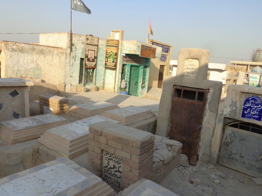 Another part of Wadi-us-Salaam cemetery. A row of three small single-storey flat-roofed buildings can be seen ahead, which might be mausoleums: large, above-ground buildings or freestanding structures designed to house multiple crypts: small, below-ground chambers or vaults, often located under a church or within a mausoleum to hold caskets.