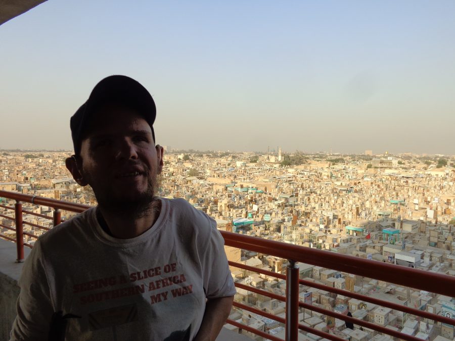 Tony in the foreground with Wadi-us-Salaam cemetery and the city of Najaf extending off towards the horizon behind. The sky is blue-grey with a slight haze.