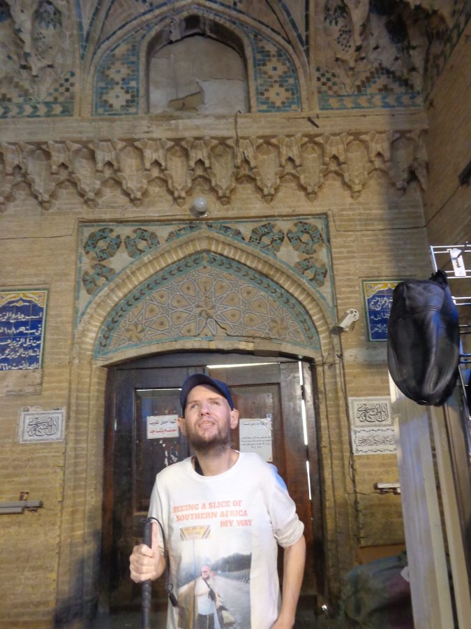 Tony inside the Al-Wazeer (Al-Wasir) Mosque with the main wooden doorway behind him. The top of the doorway and wall above are ornately decorated with tiles and brickwork. The door arch incorporates geometric decoration including 5- and 10-pointed stars. Above are mosaic tiles with simple geometric designs. The walls also display Arabic calligraphy written on blue and white tiles.