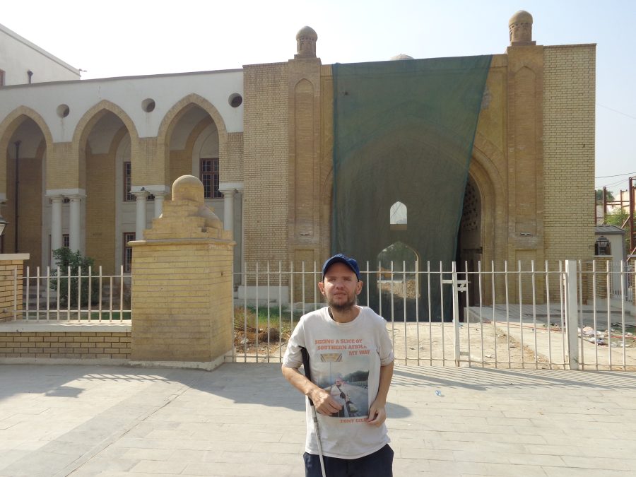 A large historic building immediately adjoining the Qushla. The building appears to have undergone recent construction or repair work but currently looks disused. It is Islamic in style. On the right side of the building is a very large pointed arch entrance currently partially covered with a green mesh. To the left are three tall but quite narrow arches supported by columns and with windows recessed within. Tony is in the foreground in front of a low wall with white painted metal railings. The building is possibly called the Palace of the Sultan or the Palace of the Ottoman Governor. 