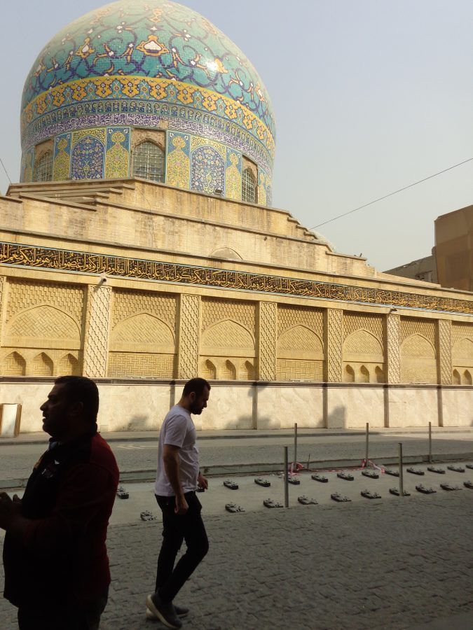 Outside Haydar-Khana Mosque showing its impressive dome covered with turquoise, blue and yellow tilework. The dome's decoration includes floral and geometric designs as well as Islamic calligraphy. Lower down there is another long strip of Islamic calligraphy written in gold on a black background. The lower stone or brick walls are carved with simpler geometric decoration with arches, alcoves and pillars. A mosque has stood here since the 12th-century. The original mosque was built by the Abbasid Caliph al-Nasir. The structure was rebuilt in the 19th-century by Mamluk Dawud Pasha and was completed in 1827. Today the mosque is one of Baghdad's most recognisable historical landmarks.