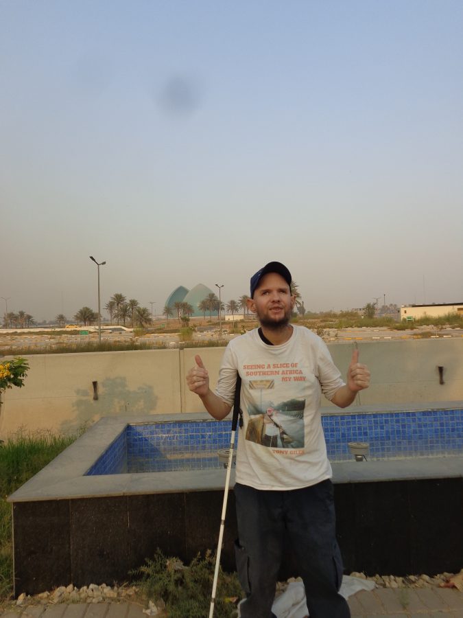 Tony with thumbs up standing in front of a low blue-tiled fountain or pool which does not contain any water. Away in the middle distance a massive turquoise dome can be seen. This is the Al-Shaheed Monument: it was originally dedicated to the Iraqi soldiers killed in the Iran–Iraq War (1980-1988) and has since grown to become generally considered to be a commemoration of all Iraqi martyrs. It was designed by Iraqi sculptor Ismail Fatah al-Turk and was opened in 1983.