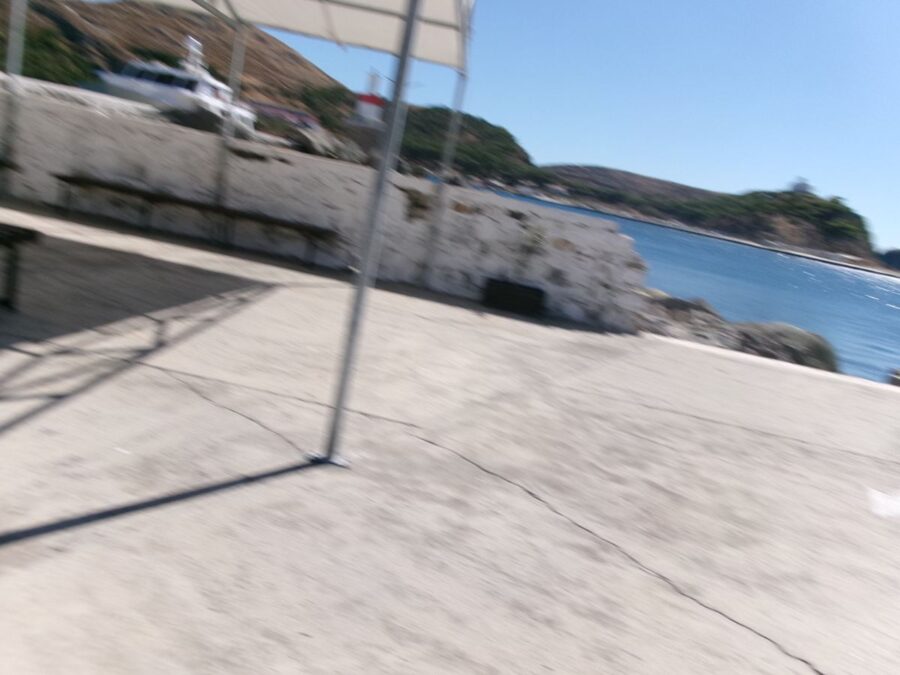 Taken at Myrina Port on Lemnos island, Greece. Tony and his partner, took the Limni Express ferry from Lemnos to Kepez, Canakkale, Türkiye. Lemnos (Limnos) is a rugged, windy, Greek island, part of the North Aegean Greek archipelago. A ferry is visible but part obscured behind a wall in front. The sea can be seen to the right.
