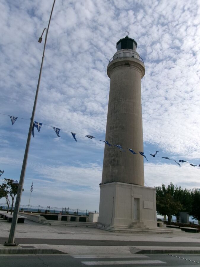 View of Alexandroupolis Lighthouse. The lighthouse is an icon of the city. It is located on the seafront promenade on the west side of the port. The lighthouse is formed of a cylindrical tower sitting on a square base with a small door. It is built from cream and grey coloured stone. At the top there is a circle of windows through which the light shines. This is topped with a small green copper dome. The structure stands at 18 metres in height making it one of the tallest lighthouses in Greece. Construction started around 1850 by the French Company of Ottoman Lighthouses and it was officially inaugurated on 1st June 1880. The light guides marine traffic travelling through the Aegean Sea between the Bosporus and the Mediterranean.